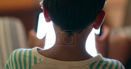 Téléchargez les photos : Jeune garçon tenant l'écran du dispositif de tablette la nuit avec une lumière bleue brillante - en image libre de droit