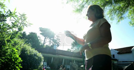 Foto de Relaxed senior lady watering plants outside in sunlight - Imagen libre de derechos