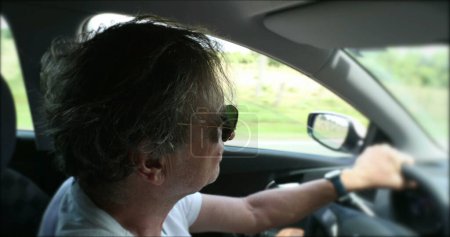 Téléchargez les photos : Older man in 70s holding steering wheel and driving on countryside road - en image libre de droit