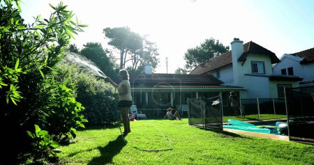 Téléchargez les photos : Person water plants with water hose in sunlight residential home garden - en image libre de droit