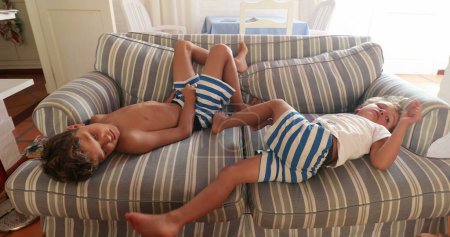 Foto de Dos niños en casa acostados en el sofá sintiéndose aburridos. Niños tumbados en el sofá en casa - Imagen libre de derechos