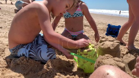 Téléchargez les photos : Enfants à la plage bâtiment château de sable avec seau - en image libre de droit