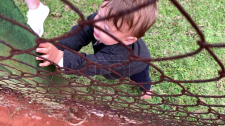 Téléchargez les photos : Bébé bébé tenant dans le fil de clôture métallique - en image libre de droit