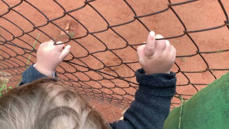 Foto de Closeup of baby hands holding intp fence watching game - Imagen libre de derechos