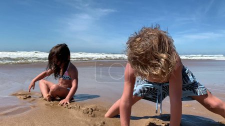 Foto de Niños hundiendo los pies en la arena en la playa. Niños jugando, hermanos y hermanas - Imagen libre de derechos