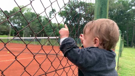 Téléchargez les photos : Baby infant holding into tennis fence watching game - en image libre de droit