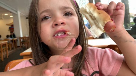 Téléchargez les photos : Enfant fille manger hotdog repas - en image libre de droit