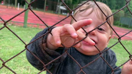 Téléchargez les photos : Baby infant holding into fence watching game from outside - en image libre de droit