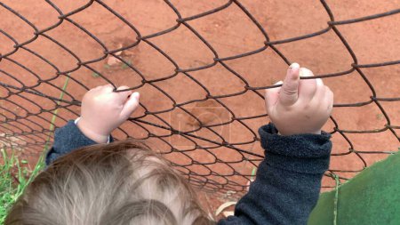 Photo for Closeup of baby hands holding intp fence watching game - Royalty Free Image