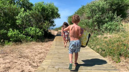 Téléchargez les photos : Enfants allant à la plage sur le sentier en bois - en image libre de droit