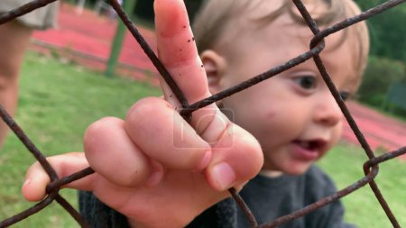 Photo for Adorable baby watching game from outside cheering, closeup little hand holding fence - Royalty Free Image