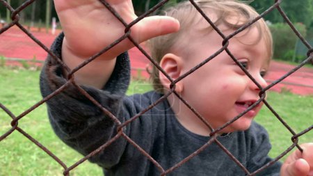 Photo for Baby infant holding into fence watching game from outside - Royalty Free Image