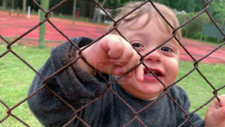 Téléchargez les photos : Baby infant holding into fence watching game from outside - en image libre de droit