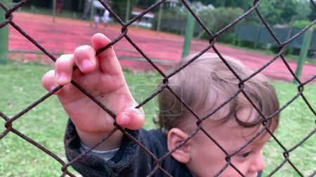 Photo for Cute baby holding into game fence watching from the outside - Royalty Free Image