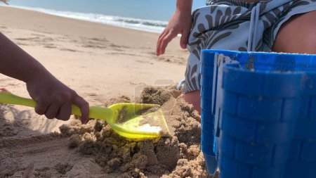 Téléchargez les photos : Enfants à la plage jouant avec le sable. Petit frère et sœur ensemble au bord de la mer - en image libre de droit
