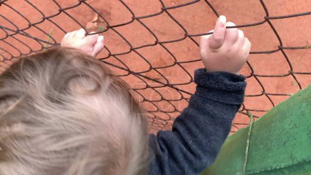 Foto de Closeup of baby hands holding intp fence watching game - Imagen libre de derechos