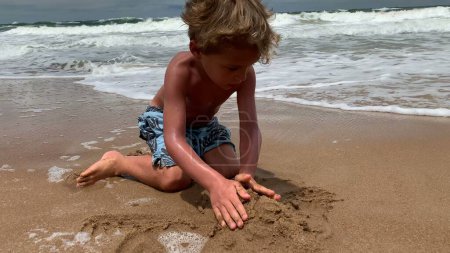 Foto de Niño niño pequeño jugando con arena en la playa orilla - Imagen libre de derechos