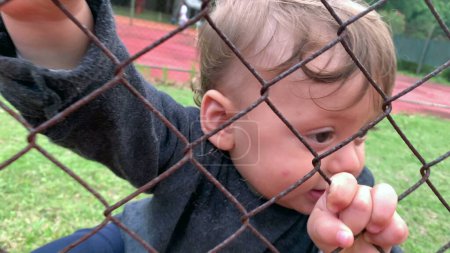 Photo for Cute baby holding into game fence watching from the outside - Royalty Free Image