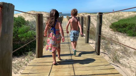 Photo for Excited kids running towards beach on wooden pathway - Royalty Free Image