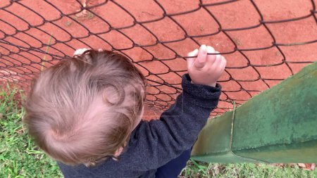 Téléchargez les photos : Bébé bébé tenant dans clôture regarder jeu - en image libre de droit
