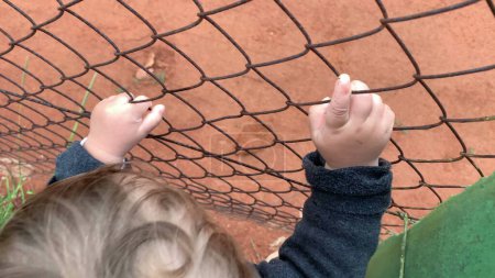 Téléchargez les photos : Bébé bébé tenant dans clôture regarder jeu - en image libre de droit