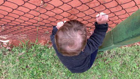 Photo for Infant baby holding into fence watching game - Royalty Free Image