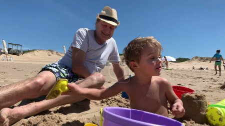 Téléchargez les photos : Famille à la plage jouant avec le sable, grand-père et enfant ensemble - en image libre de droit