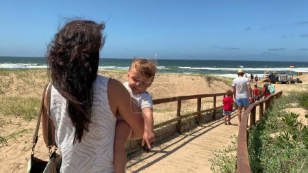 Foto de Familia yendo a la playa, madre llevando al bebé en brazos caminando camino de madera - Imagen libre de derechos