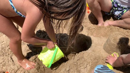 Téléchargez les photos : Famille à la plage jouant avec la construction de sable château de sable avec seau - en image libre de droit
