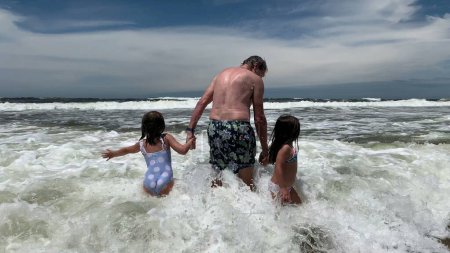 Foto de Abuelo sosteniendo las manos de nietas en la playa - Imagen libre de derechos