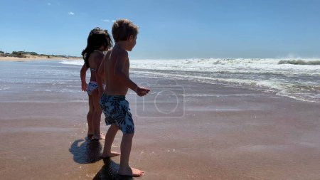 Foto de Niños felices en la playa saltando arriba y abajo sintiéndose extáticos, niño y niña en la orilla - Imagen libre de derechos