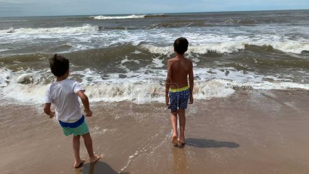 Téléchargez les photos : Les enfants à la plage étant ludique fuyant les vagues d'eau - en image libre de droit