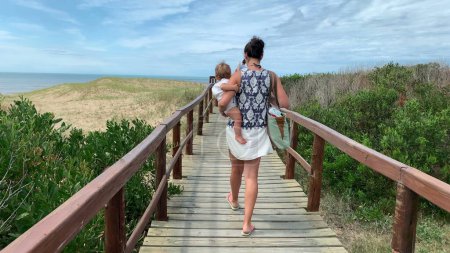 Photo for Mother holding baby walking towards beach on pathway - Royalty Free Image