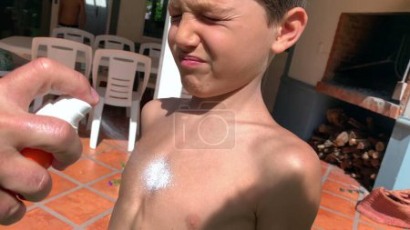 Foto de Padre rociando loción bloqueadora solar al pecho del niño - Imagen libre de derechos