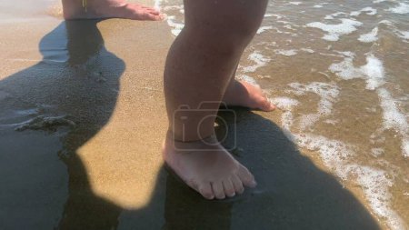 Photo for Barefoot adorable baby feet and toes feeling beach water at sea shore - Royalty Free Image