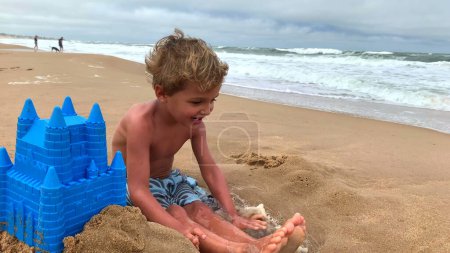 Foto de Niño pequeño jugando en la playa con pala y cubo en la orilla - Imagen libre de derechos