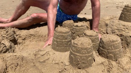 Photo for Older man building sandcastle at beach - Royalty Free Image