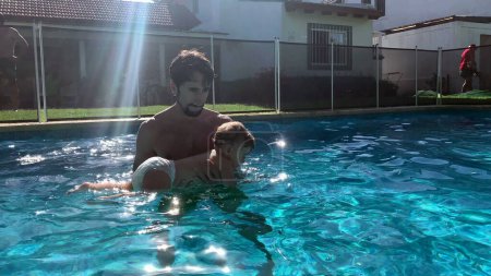 Téléchargez les photos : Père tenant bébé à la piscine, enfants jouant pendant la journée d'été - en image libre de droit