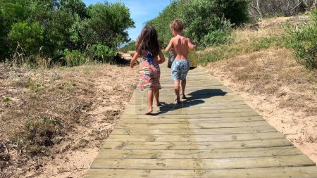 Téléchargez les photos : Enfants allant à la plage sur le sentier en bois - en image libre de droit
