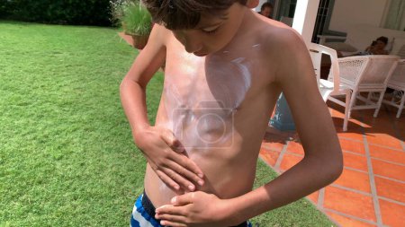 Foto de Niño frotando protector solar al cuerpo durante el día de verano. bronceado prevención - Imagen libre de derechos