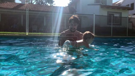 Foto de Padre enseñando a los bebés a nadar en la piscina durante el verano en casa - Imagen libre de derechos