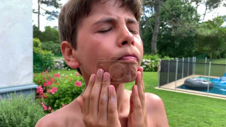 Téléchargez les photos : Jeune garçon applique crème solaire face à face - en image libre de droit