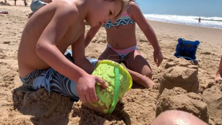 Téléchargez les photos : Enfants à la plage bâtiment château de sable avec seau - en image libre de droit