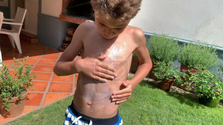Téléchargez les photos : Enfant frottant crème solaire dans la poitrine du corps. Jeune garçon appliquant une protection solaire - en image libre de droit