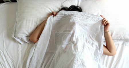 Photo for Funny young woman playing hide and seek peekaboo under blanket in bed - Royalty Free Image