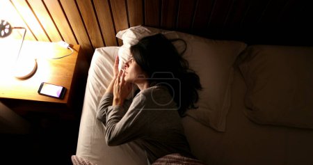 Photo for Woman lying in bed turns off smartphone and bedside nightstand lamp - Royalty Free Image