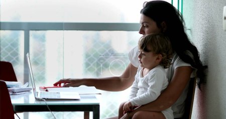 Téléchargez les photos : Mother watching content online with baby toddler on lap - en image libre de droit