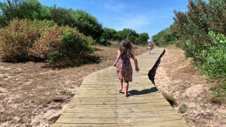 Téléchargez les photos : Little girl child running towards beach or wooden pathway - en image libre de droit