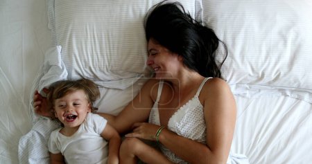 Téléchargez les photos : Mother waking up in the morning, baby getting in bed with mom. Mom infant love and affection - en image libre de droit
