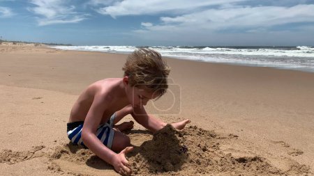 Foto de Niño jugando con arena en la playa en vacaciones de verano - Imagen libre de derechos
